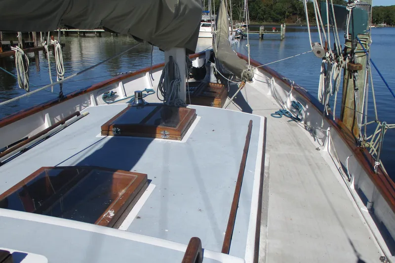 Slide: The Image of 1955 Custom Gaff Rigged Ketch with full keel, docked in a serene marina setting. - 23