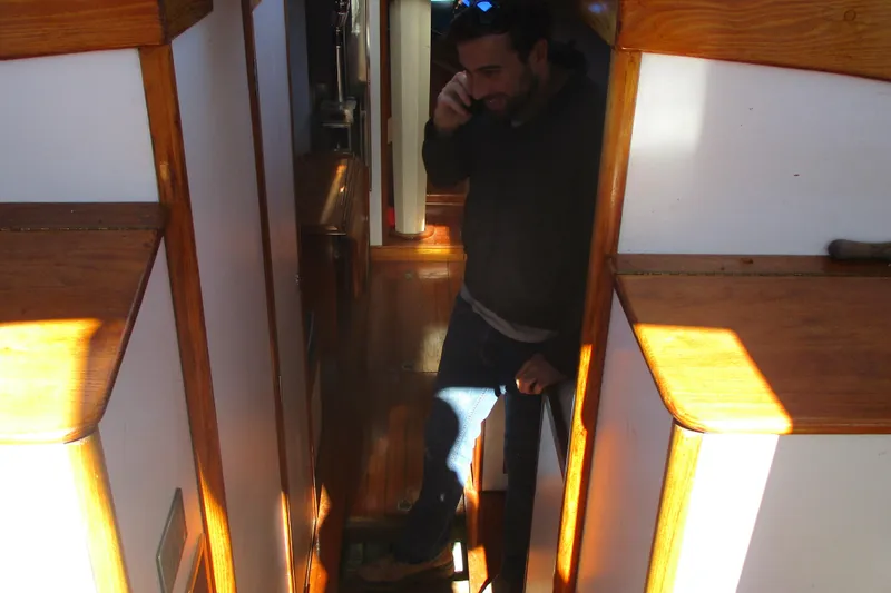 Slide: The Image of Man on phone inside 1955 Custom Gaff Rigged Ketch, wooden interior, natural light. - 25