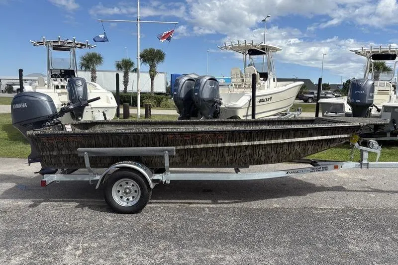 Slide: The Image of 2026 SeaArk DXS 1652 DKLD boat on trailer, parked with other boats, under blue sky. - 5