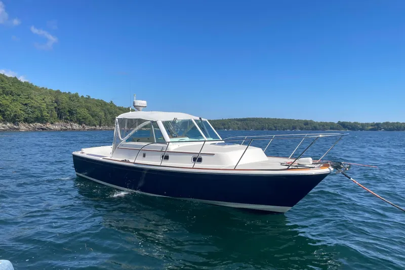 The Image of 2012 Hunt Surfhunter boat on calm water with forested shoreline. - 1