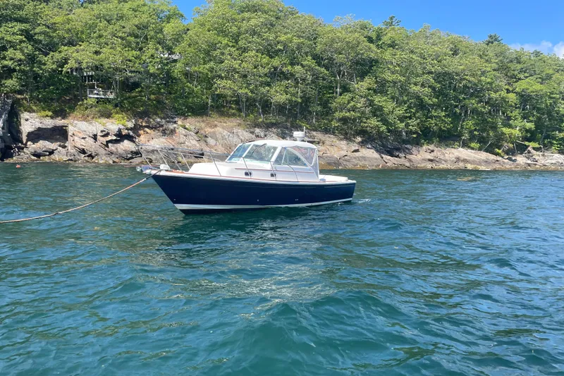 Slide: The Image of 2012 Hunt Surfhunter boat anchored near rocky shoreline with lush greenery. - 12