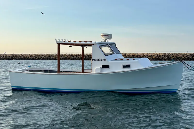 Slide: The Image of 1980 SISU 26 boat on calm water near rocky shoreline, under clear sky. - 1