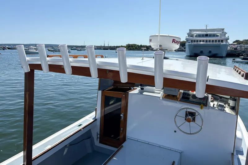 Slide: The Image of 1980 SISU 26 boat with rod holders, docked in a marina with a large ship nearby. - 10