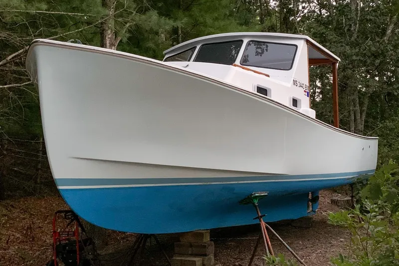 Slide: The Image of 1980 SISU 26 boat on land, white and blue hull, surrounded by trees. - 7