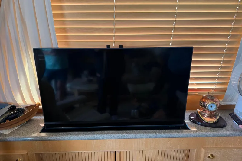 Slide: The Image of Flat-screen TV on a wooden cabinet with blinds and a decorative clock nearby. - 5