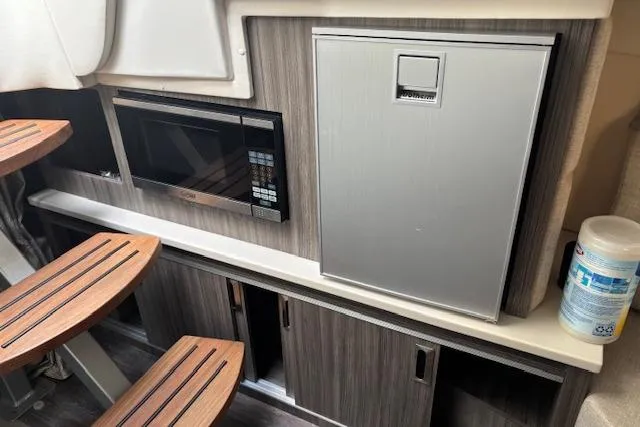 Slide: The Image of 2024 Sea Ray Sundancer 320 interior with microwave, fridge, and wooden cabinetry. - 12
