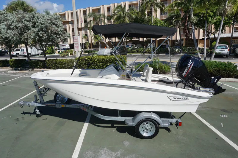 Slide: The Image of 2026 Boston Whaler 130 Super Sport boat on trailer in sunny parking lot. - 1