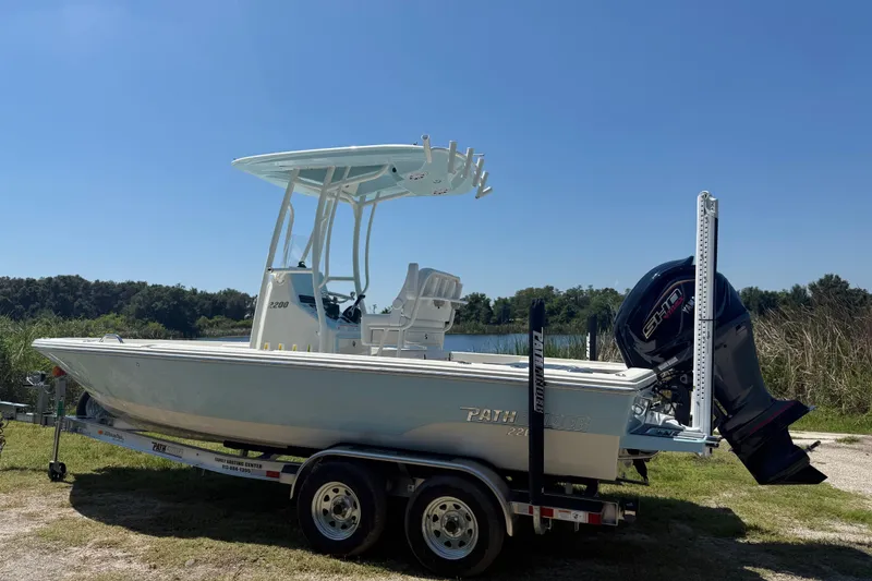 Slide: The Image of 2026 Pathfinder 2200 TRS boat on trailer, parked near a lake under clear blue sky. - 2