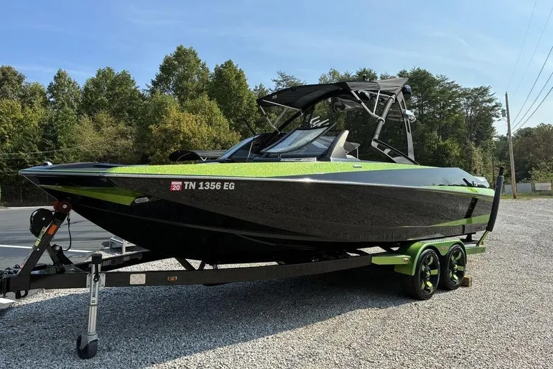 Slide: The Image of 2014 Axis A24 boat on trailer, black and green, parked on gravel. - 2
