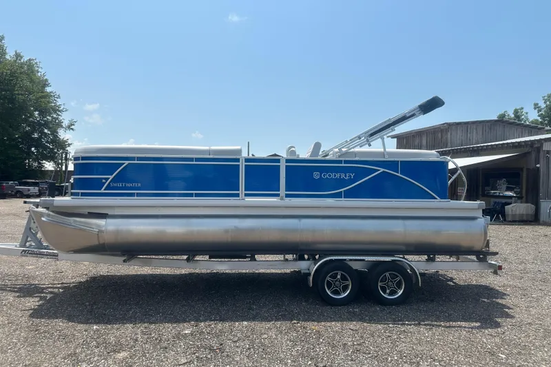 Slide: The Image of 2024 Godfrey SWEETWATER 2286 SB pontoon boat on trailer, parked outdoors. - 2
