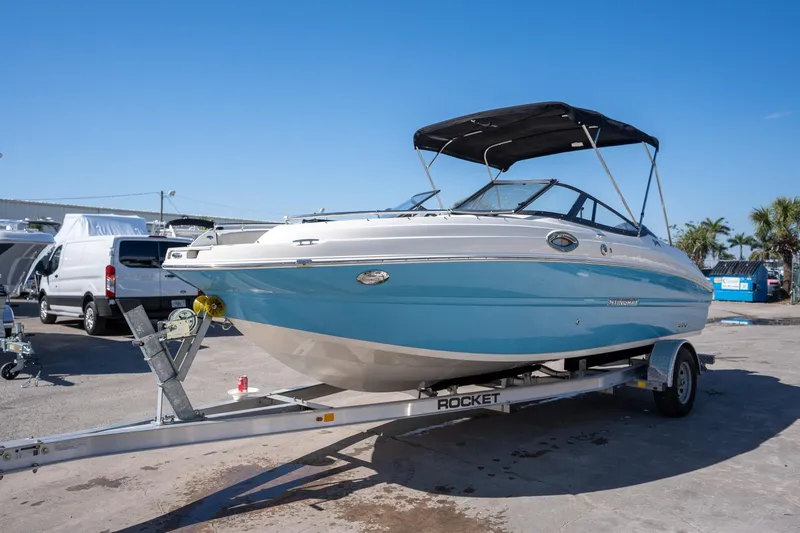 The Image of 2024 Stingray 211DC boat on trailer, blue and white design, parked outdoors. - 1
