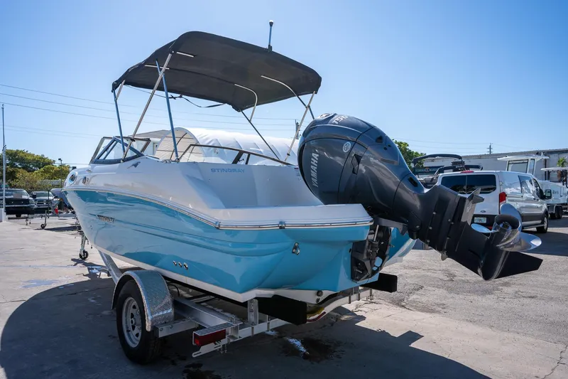 Slide: The Image of 2024 Stingray 211DC boat with outboard motor on trailer, parked outdoors. - 14
