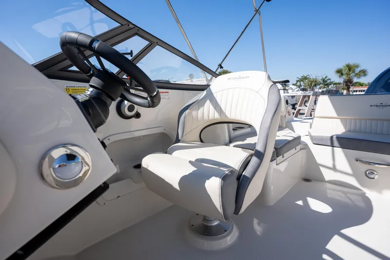 Slide: The Image of 2024 Stingray 211DC boat interior with steering wheel and captain's chair, under clear blue sky. - 9
