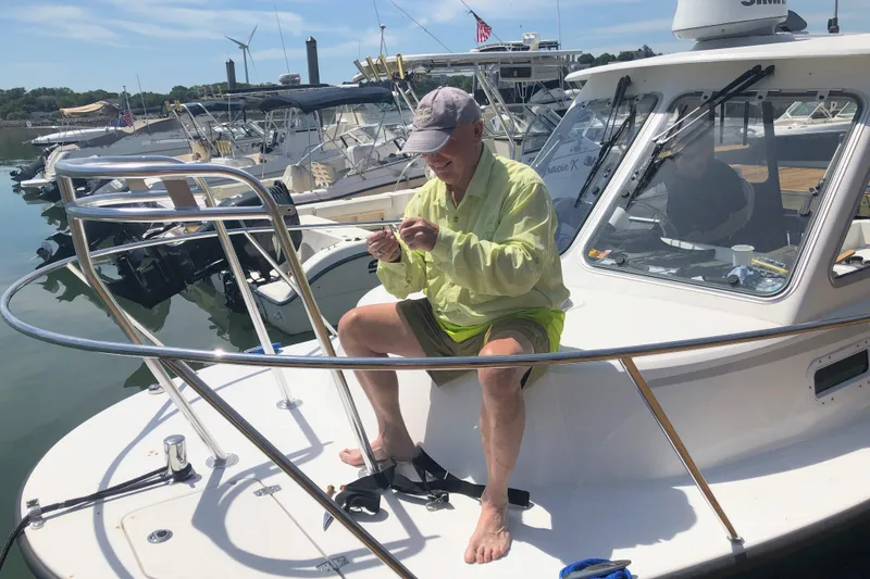 Slide: The Image of Man sitting on a 2020 Maritime 23 Challenger boat, preparing fishing gear at a marina. - 11