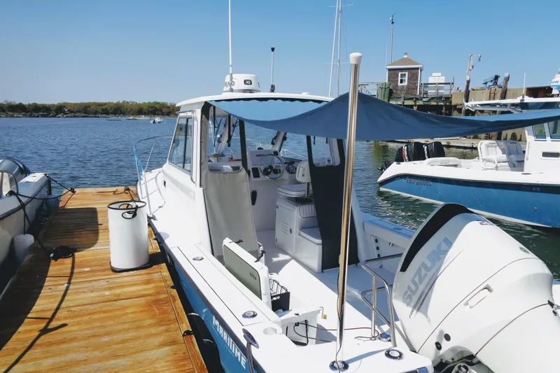Slide: The Image of 2020 Maritime 23 Challenger boat docked with Suzuki engine, blue canopy, and scenic waterfront. - 4