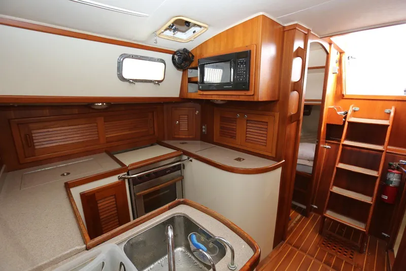 Slide: The Image of Interior of 2004 Pacific Seacraft 40 sailboat, featuring a compact kitchen with wooden cabinetry. - 24