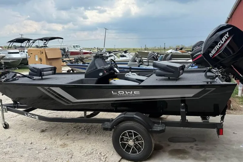 Slide: The Image of 2026 Lowe Skorpion 16 boat with Mercury engine on trailer, parked outdoors. - 0