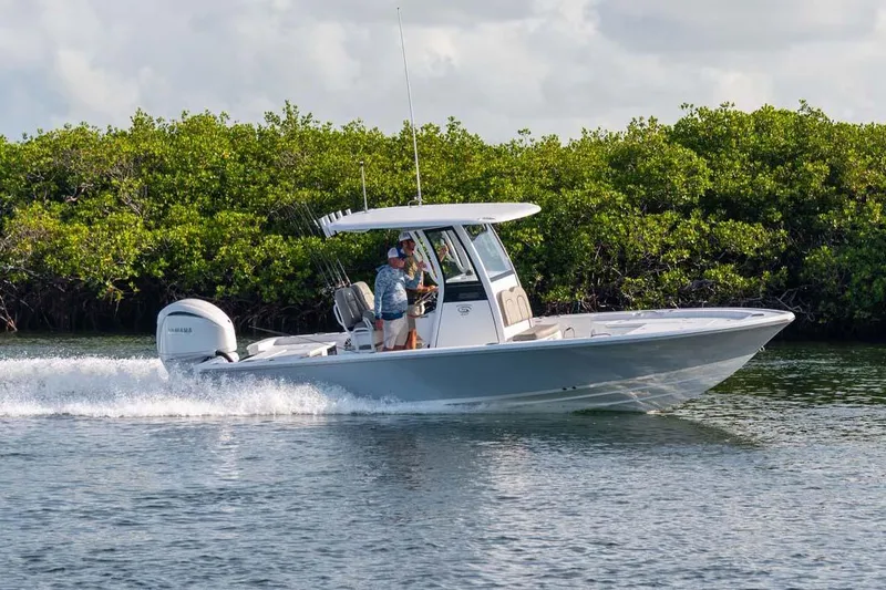 Slide: The Image of Manufacturer Provided Image: 2025 Sportsman Masters 247 Bay Boat cruising on water near lush greenery. - 2