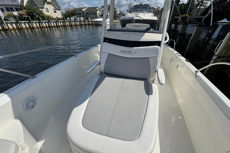 Slide: The Image of 2015 Boston Whaler 270 Dauntless boat interior with cushioned seating, docked by waterfront homes. - 7