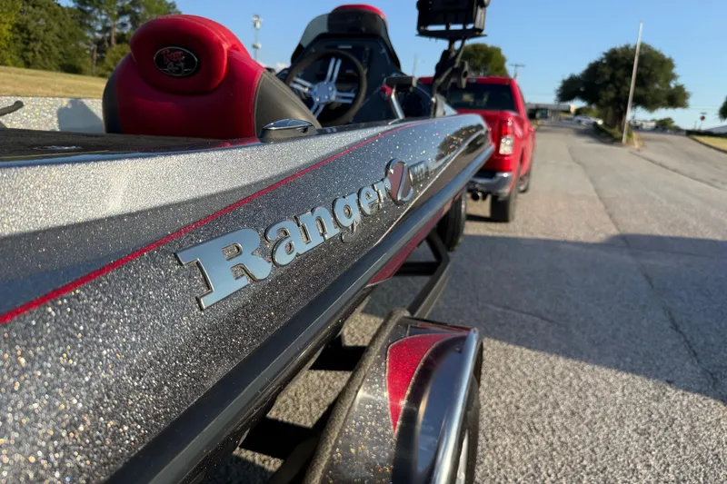 Slide: The Image of 2013 Ranger Z117 boat with red and gray seats, set in a grassy landscape. - 28