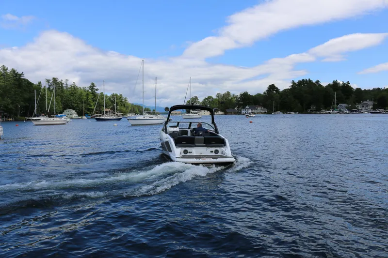 Slide: The Image of 2026 Scarab 255 LX boat cruising on a scenic lake with sailboats and trees. - 2