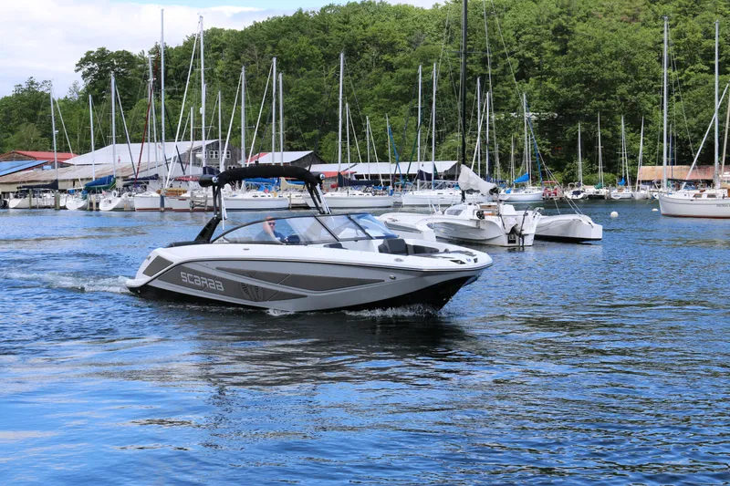 Slide: The Image of 2026 Scarab 255 LX boat cruising in a marina with sailboats and lush greenery. - 3