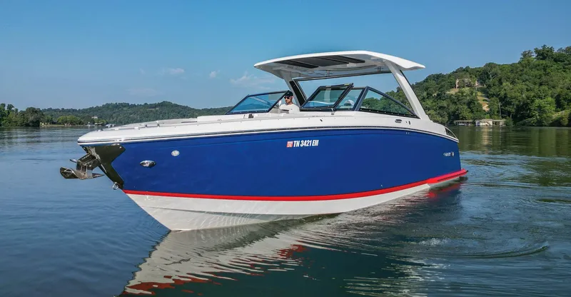 Slide: The Image of 2023 Cobalt R33 boat cruising on a calm lake with lush green hills. - 12