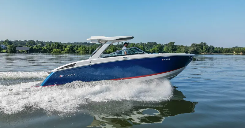 Slide: The Image of 2023 Cobalt R33 boat cruising on a calm lake with lush green shoreline. - 6