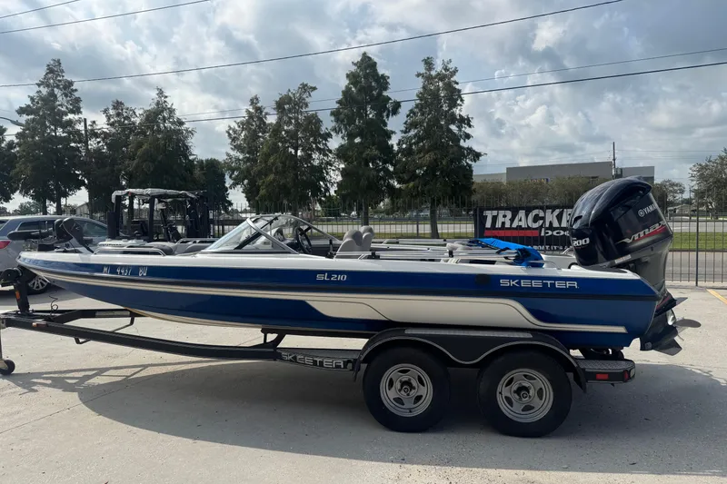 Slide: The Image of 2012 Skeeter SL210 boat on trailer, blue and white, parked outdoors. - 7