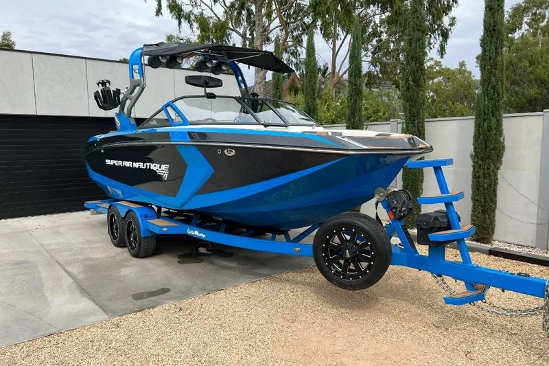 Slide: The Image of 2018 Nautique Super Air Nautique G23 boat on trailer, blue and black design. - 0
