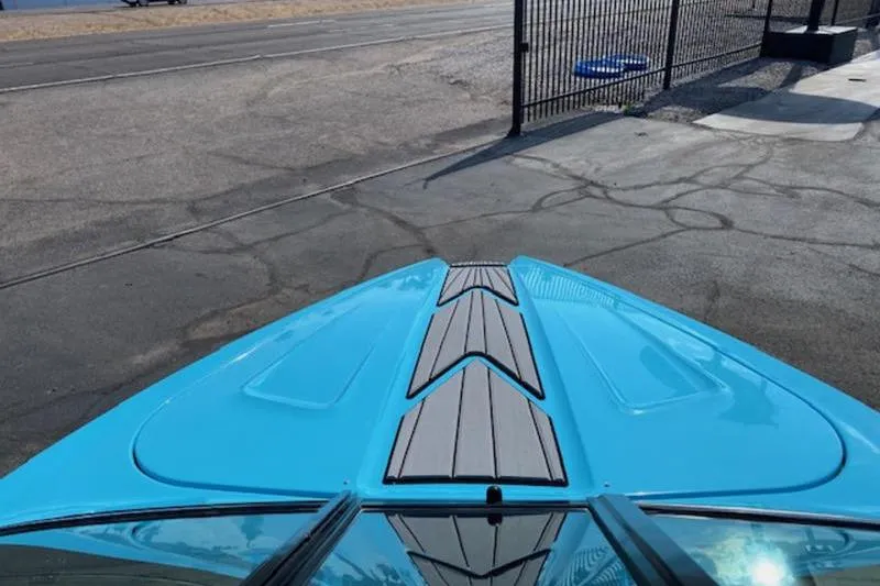 Slide: The Image of 2018 MasterCraft ProStar boat with blue deck, parked on pavement near a fence. - 2