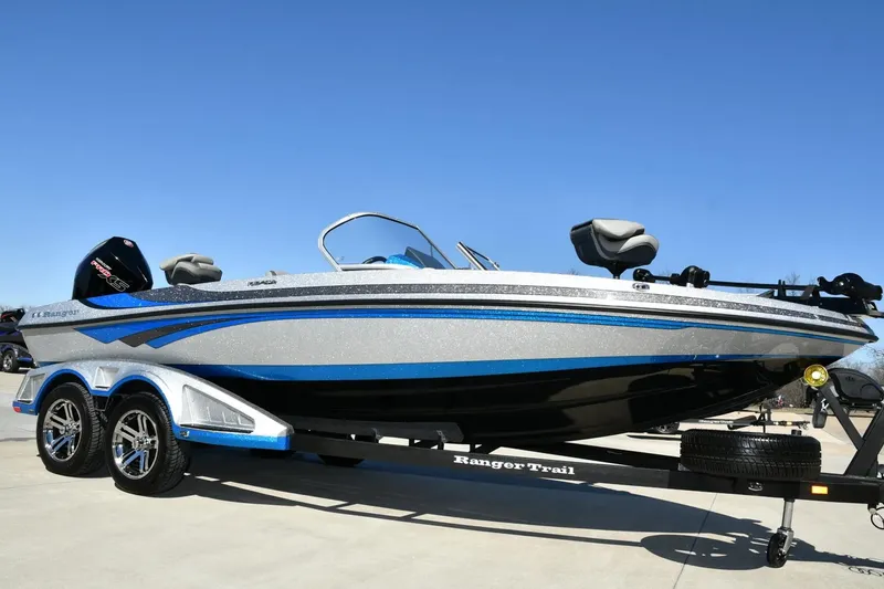 Slide: The Image of 2024 Ranger 212LS Reata boat on trailer, blue and silver design, clear sky background. - 0