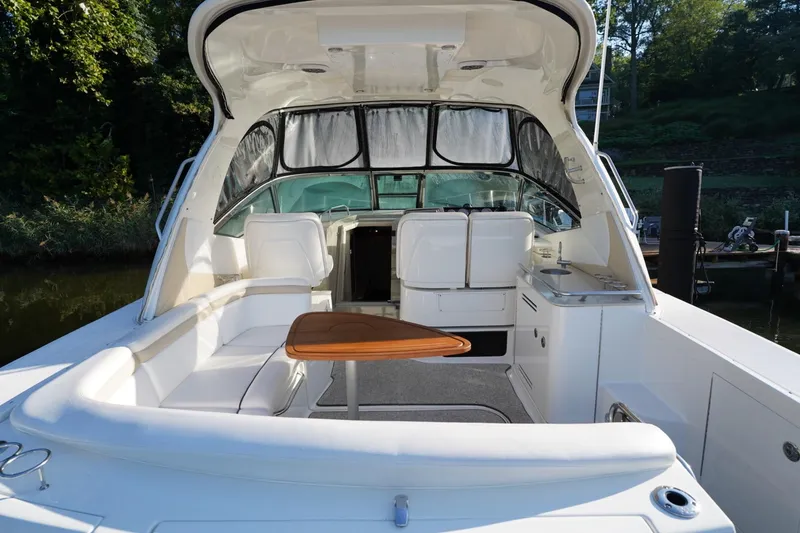 Slide: The Image of 2010 Sea Ray 370 Sundancer boat interior with seating and table, docked by lush greenery. - 20