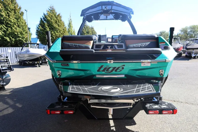Slide: The Image of 2024 Tigé Ultré 25ZX boat, rear view, vibrant teal color, parked outdoors. - 11