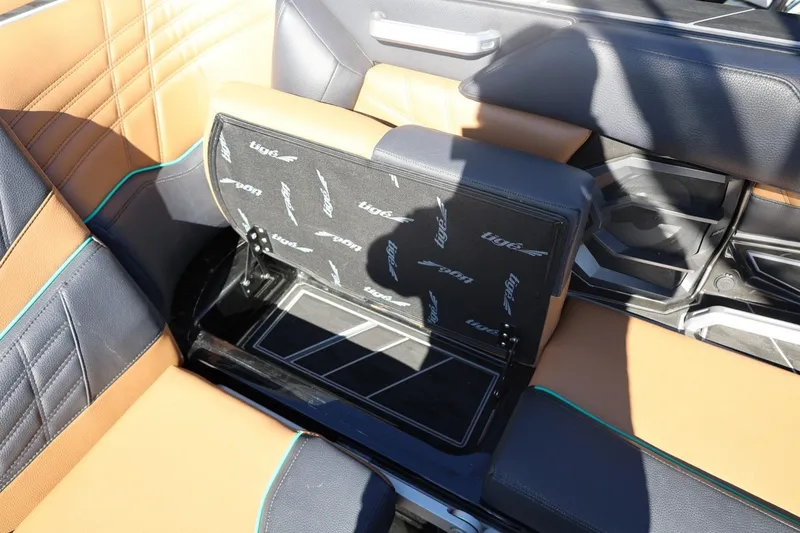 Slide: The Image of 2024 Tigé Ultré 25ZX boat interior with tan and black seating, open storage compartment. - 51