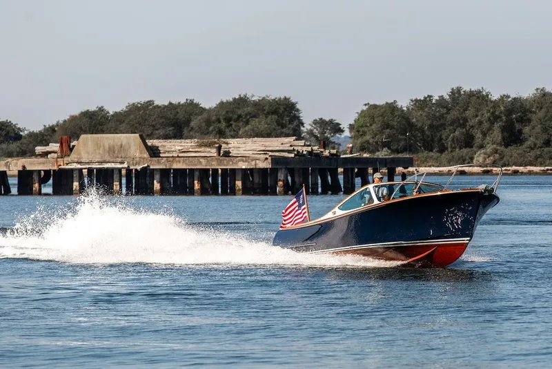 Slide: The Image of 2003 Hinckley T29R boat cruising on water near a pier, American flag displayed. - 19