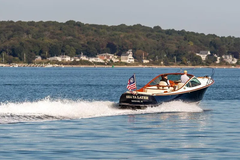 Slide: The Image of 2003 Hinckley T29R boat cruising on a serene lake with scenic shoreline backdrop. - 21