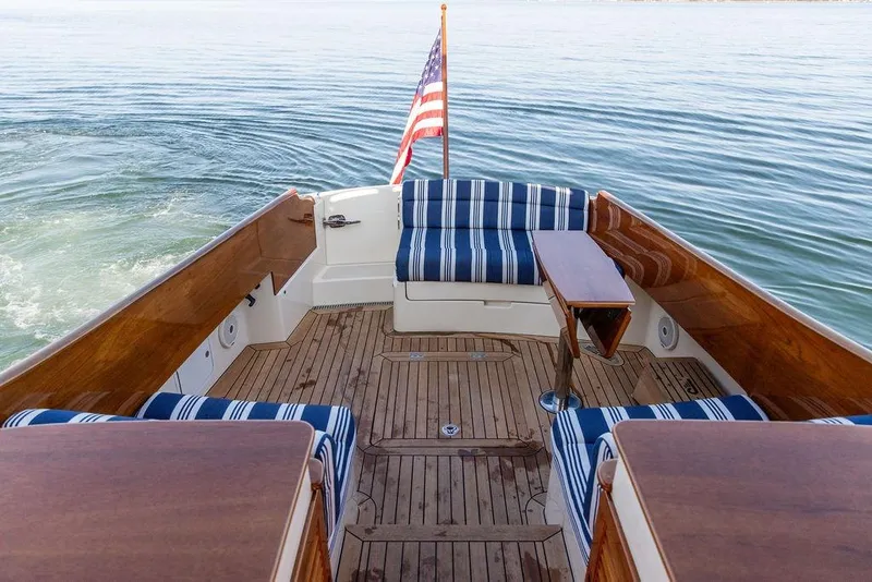 Slide: The Image of Hinckley Picnic Boat MKIII 2017 with striped seating, wooden deck, and American flag on calm water. - 13
