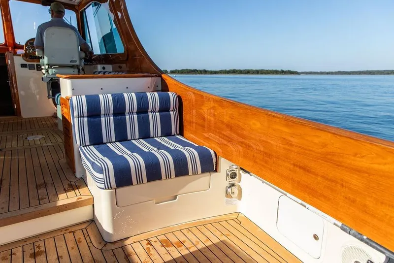 Slide: The Image of 2017 Hinckley Picnic Boat MKIII interior with striped seating, wooden deck, and ocean view. - 16