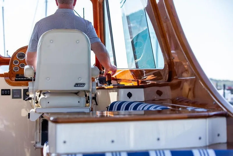 Slide: The Image of 2017 Hinckley Picnic Boat MKIII interior with captain at helm, featuring polished wood and striped seating. - 25