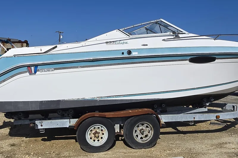 Slide: The Image of 1992 Wellcraft Eclipse 233 boat on trailer, white and blue design, clear sky background. - 7