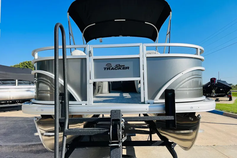 Slide: The Image of 2026 Sun Tracker Fishin' Barge 22 DLX pontoon boat, silver exterior, docked under clear blue sky. - 2