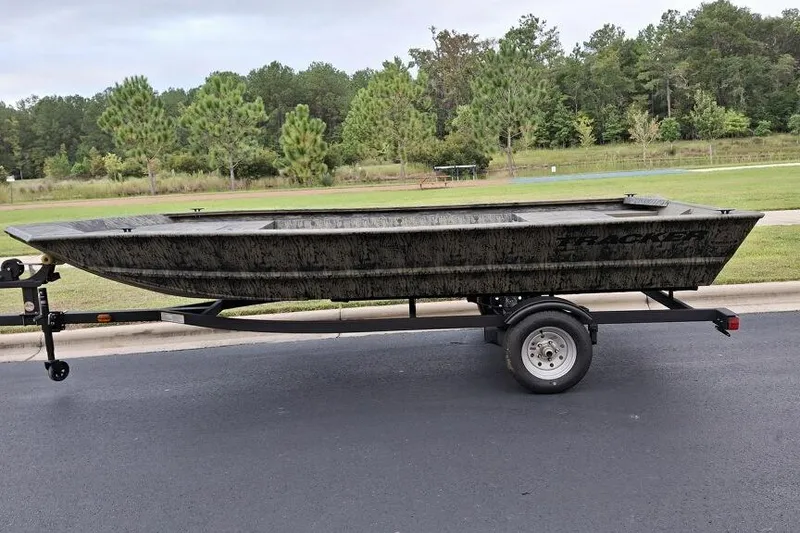 The Image of 2026 Tracker Grizzly 1648 Utility boat on trailer, parked on roadside with trees in background. - 0