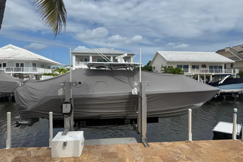 Slide: The Image of Covered 2024 Contender 32 ST boat on lift, dockside with waterfront homes in background. - 19