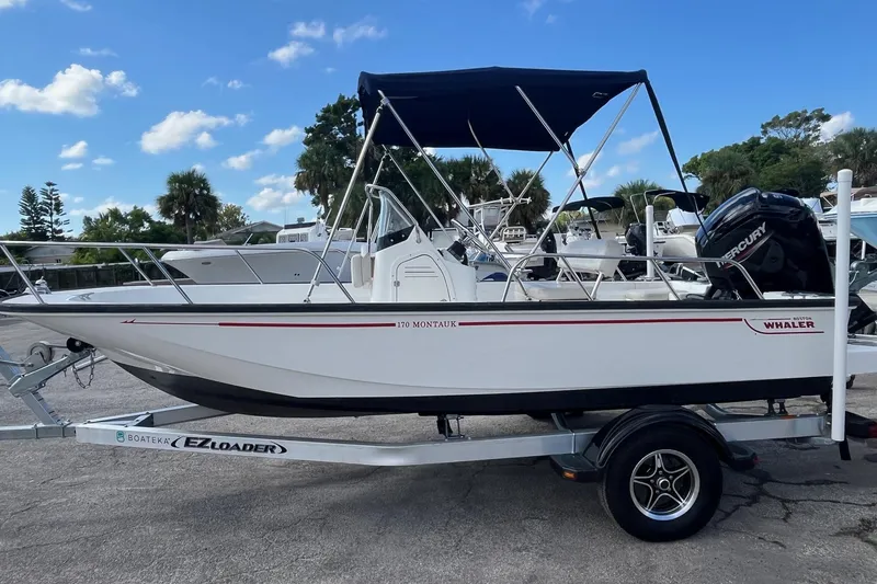 Slide: The Image of 2022 Boston Whaler 170 Montauk boat on trailer, with canopy, parked outdoors. - 0