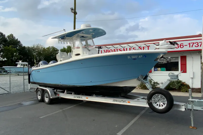 Slide: The Image of 2023 Cobia 262 Center Console boat on trailer at dealership, blue hull, dual engines. - 5