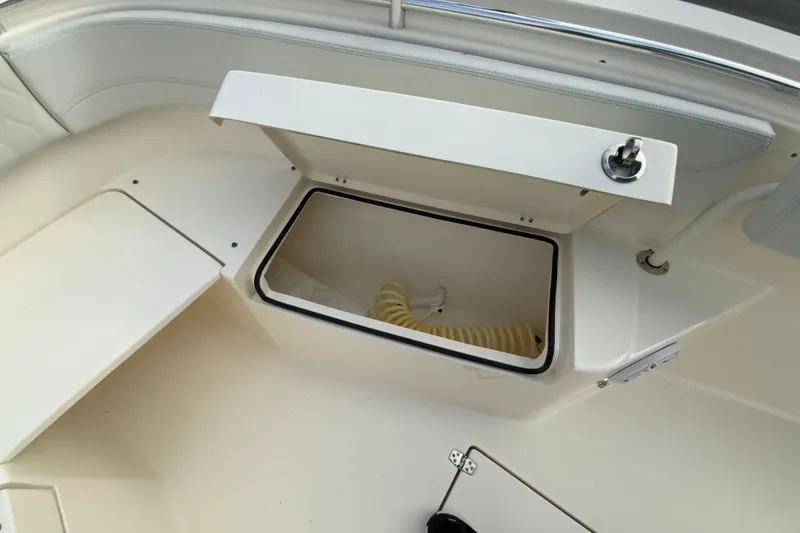 Slide: The Image of 2023 Cobia 262 Center Console boat storage compartment with open lid and hose inside. - 67