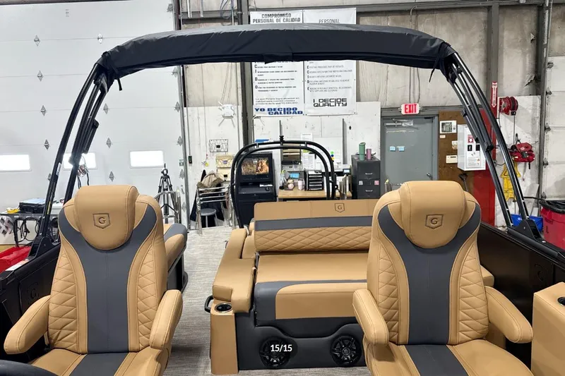 Slide: The Image of 2026 Godfrey Monaco 23' Tritoon interior with tan and gray seating in a workshop setting. - 15