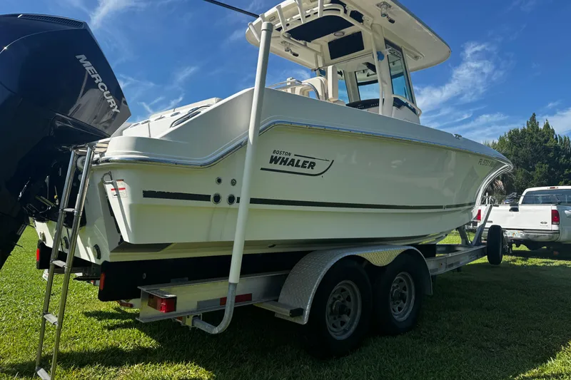 Slide: The Image of 2019 Boston Whaler 26 Outrage boat on trailer, parked on grass under blue sky. - 20