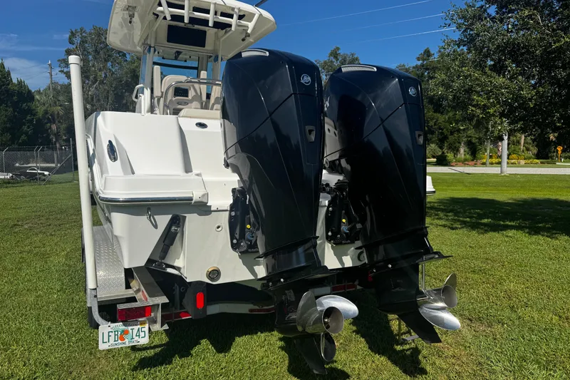 Slide: The Image of 2019 Boston Whaler 26 Outrage with dual outboard engines on a trailer, parked on grass. - 21